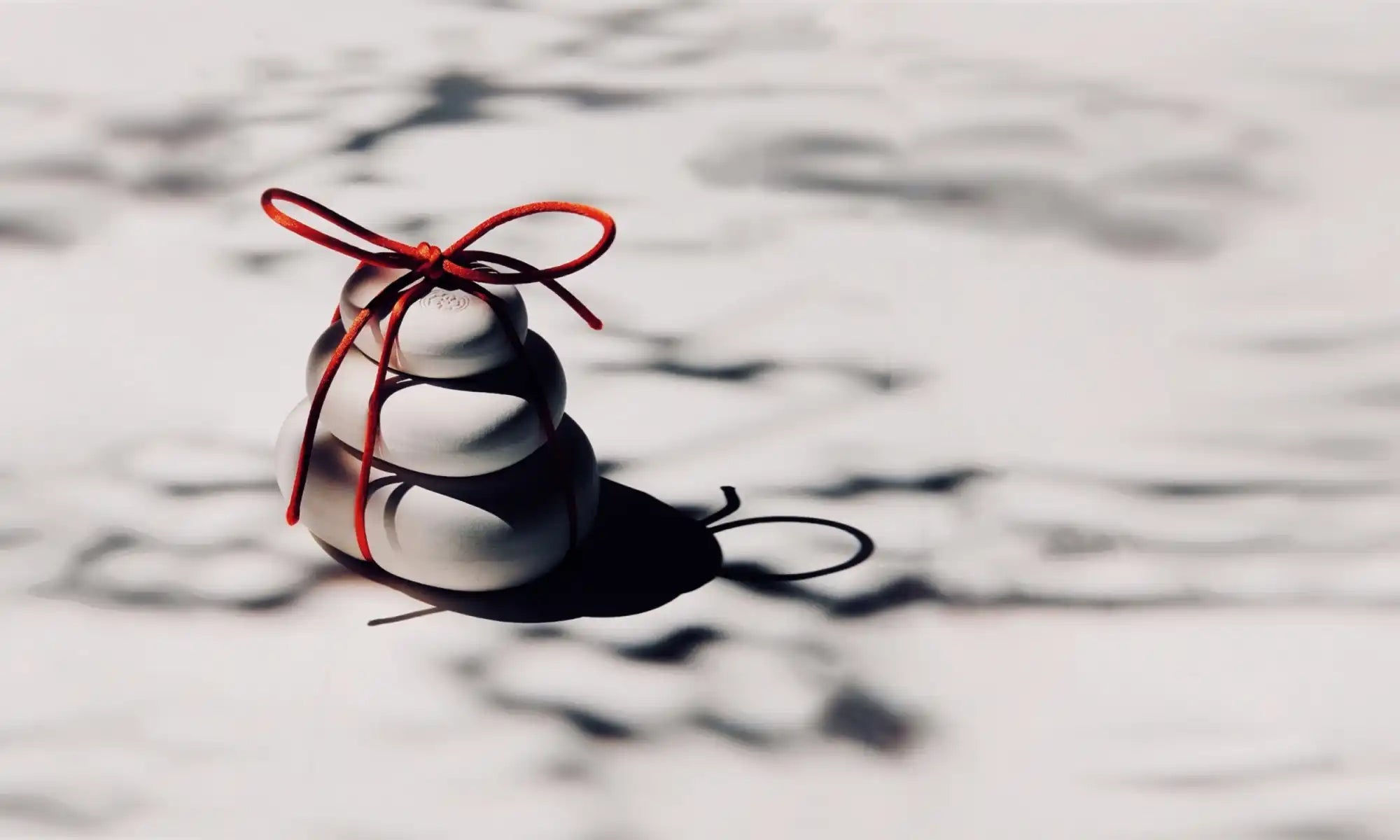 A stack of three white, rounded, irregular stones tied with a red string.